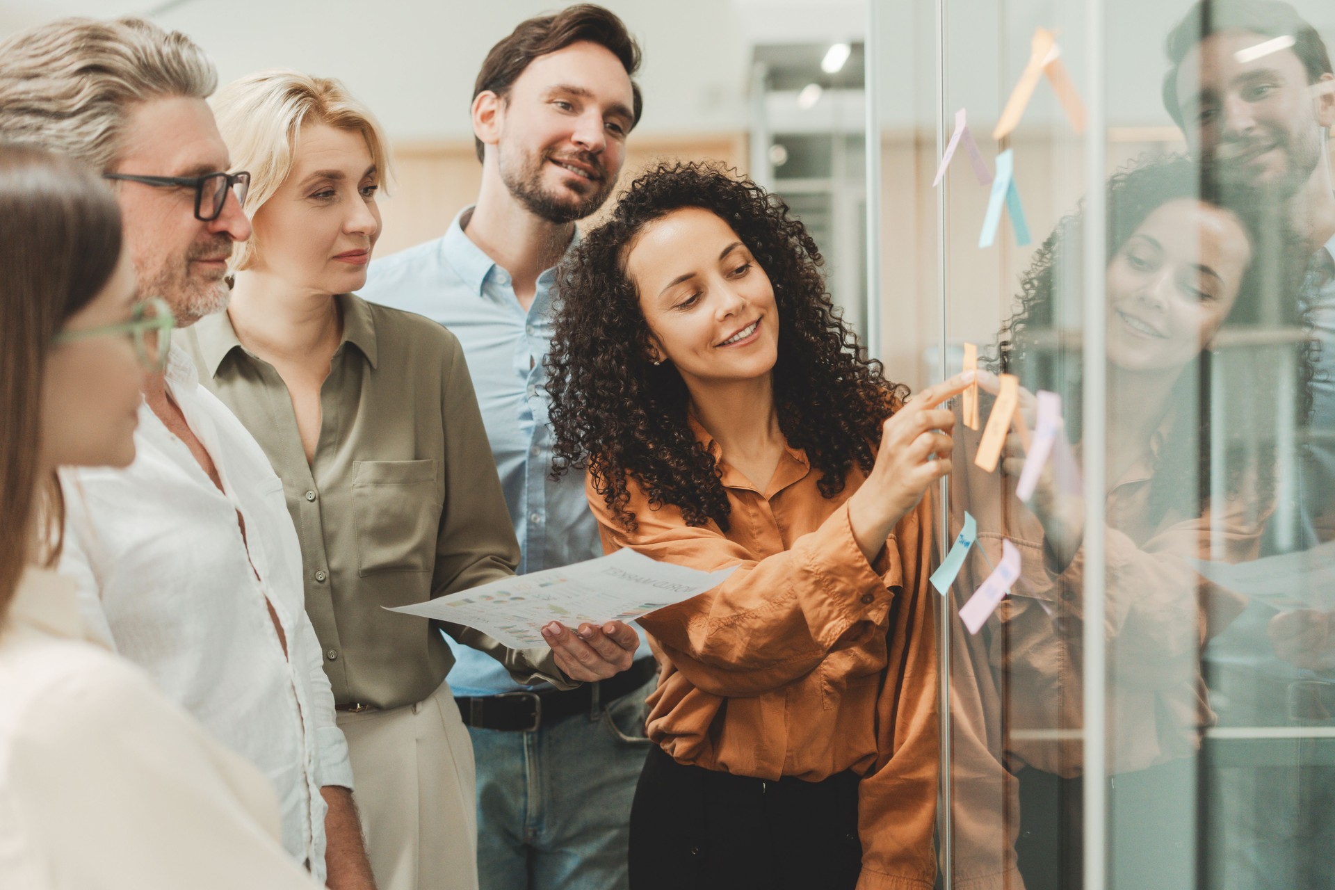 Scrum master talking with colleague using sticky notes, agile methodology for productivity. Group smiling business people working together in modern office. Teamwork, scrum concept